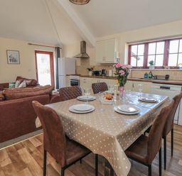 A kitchen and dining area with a table set for four people with chairs and a living area with sofas near Curlew Cottage near Filey