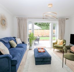 A living room with a blue sofa green armchairs a wall mirror and a round dining table at Pine Cottage in Wrentham