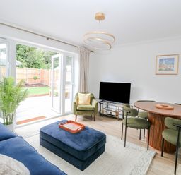 A living room with blue sofa green armchair round dining table and open patio doors at Pine Cottage in Wrentham