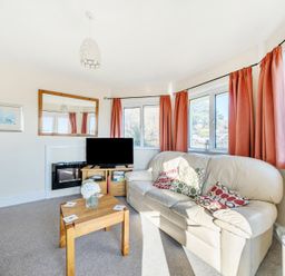 A living room with a white leather sofa pink curtains a wooden coffee table and a television at Bayview in Overcombe near Preston