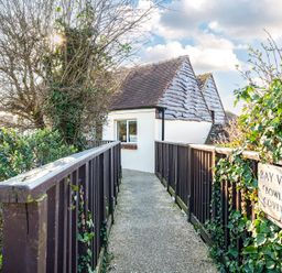 A narrow pathway with wooden railings leading to a small building with tiled roofs at Bayview Overcombe near Preston