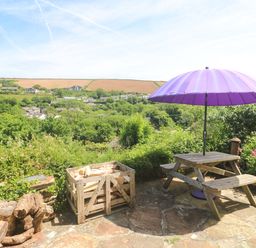 A garden with a purple umbrella and wooden table at Greenways in Perranporth