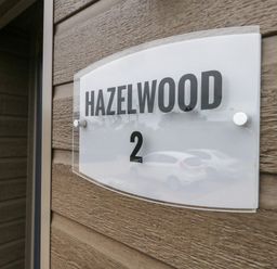 A wall-mounted sign with the text Hazelwood 2 on a wooden exterior wall at Hazelwood 2 Pinewood near Lyme Regis