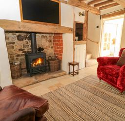 A living room with a wood stove and red sofa at 8 Gloucester Street in Winchcombe