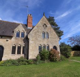 An old stone house with black windows and doors surrounded by bushes and a grassy lawn at The Alms House East in Forthampton near Tewkesbury