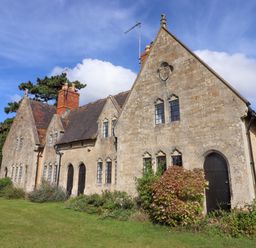 Exterior view of a stone building with gothic windows and chimneys surrounded by greenery at The Alms House East in Forthampton near Tewkesbury
