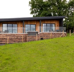 A modern wooden house with glass balcony railings and outdoor seating on a grassy hillside at The Lookout in Longridge