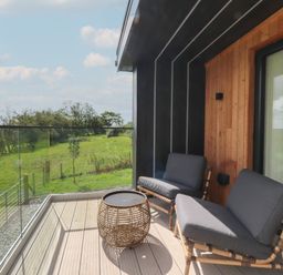 A balcony with two chairs and a round table overlooking a green field at The Lookout in Longridge