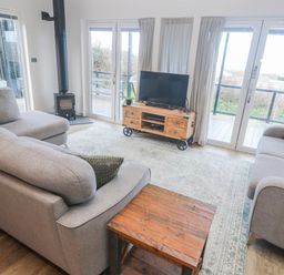 A living room with a sofa, television, and wood stove at Bay View in Portreath