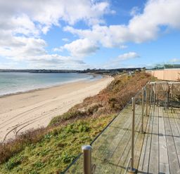 A wooden deck with glass railing and bar stools overlooking a sandy beach and sea at The Warren M45 in Abersoch