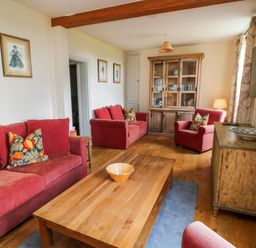 A living room with red sofas wooden furniture and framed pictures at Ivy Cottage in Colerne