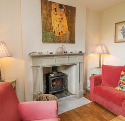 A living room with a wood burning stove fireplace two red sofas lamps and paintings at Ivy Cottage in Colerne