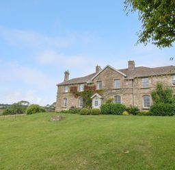 A stone house with ivy on the walls and a lawn in front at Peartree in Colerne