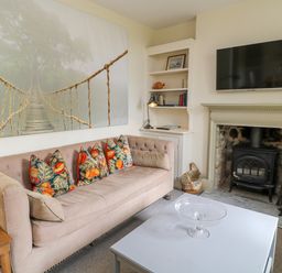 A living room with a beige sofa and patterned cushions a white coffee table a fireplace with a wood stove a mounted TV and built in shelves at Peartree in Colerne