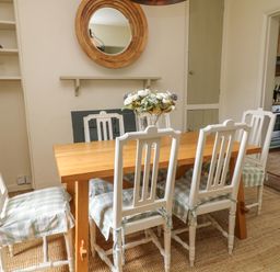 A dining area with a wooden table and six white chairs with checkered seat cushions at Peartree in Colerne