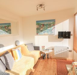 A living room with a yellow sofa with pillows a wall-mounted television a small white table and wooden blinds at 418 Norton Park in Dartmouth