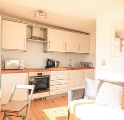A kitchen with white cabinets a stove microwave kettle toaster and a dining table with a chair at 418 Norton Park Dartmouth