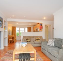 An open living room with two sofas a wooden coffee table a dining table and chairs with a kitchen in the background at Bryher in Trebetherick near Polzeath