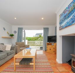 A living room with a sofa armchair coffee table and wood stove at Bryher in Trebetherick near Polzeath