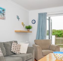 A living room with a sofa armchair coffee table and open glass door leading to a garden at Bryher in Trebetherick near Polzeath