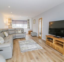 A living room with a grey sectional sofa a wooden TV stand and a large flat screen TV at Melin Y Plas in Llanaber