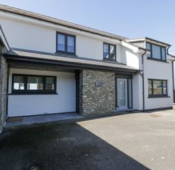 The exterior front view of a white two-story house with black-framed windows and a stone wall section at Melin Y Plas in Llanaber