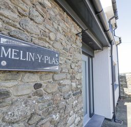 Stone wall with a Melin Y Plas sign next to a doorway and paved area outside at Melin Y Plas in Llanaber