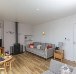 A living room with sofas a wood stove a television on a wooden stand and a table with flowers at Rowena in Mullion