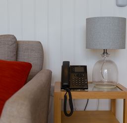 A side table with a telephone and a glass lamp next to a gray sofa with red and yellow cushions at Rowena in Mullion