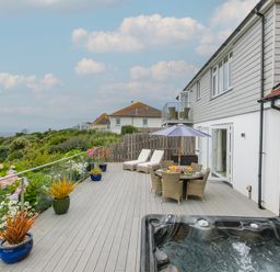 A large outdoor patio with a hot tub dining table with umbrella and lounge chairs overlooking greenery at Morwenna in Mullion