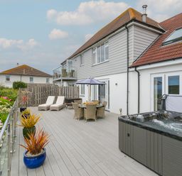 A large outdoor deck with lounge chairs a dining table with an umbrella potted plants and a hot tub at Morwenna in Mullion
