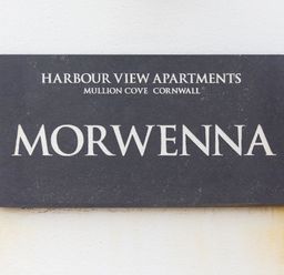 A black sign with white text reading Harbour View Apartments Mullion Cove Cornwall Morwenna