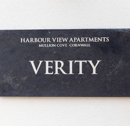 A black sign with white text reading Harbour View Apartments Mullion Cove Cornwall Verity
