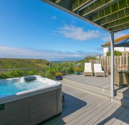 An outdoor deck area with a hot tub two lounge chairs dining table with chairs and an umbrella at Verity in Mullion