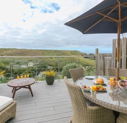An outdoor patio with a wicker dining set and umbrella overlooking green hills at Daphne in Mullion