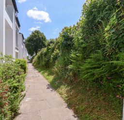 A paved walkway bordered by buildings on one side and dense greenery on the other at 37 Tamar in St Ann's Chapel near Callington