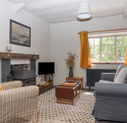 A living room with a striped armchair a gray sofa a wooden fireplace a window with yellow curtains and a patterned rug at Hole Farm Stables in Bickington near Ashburton