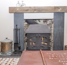 A fireplace with a metal wood stove and fireplace tools on the side at Hole Farm Stables in Bickington near Ashburton