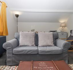 A living room with a grey sofa and cushions a floor lamp and a chair next to a cabinet with a table lamp at Hole Farm Stables in Bickington near Ashburton