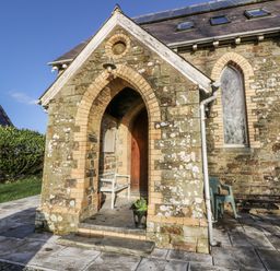 An exterior entrance with an arched doorway and chair at Church Llygad Y Dyffryn Sarnau near Brynhoffnant