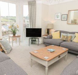A living room with gray sofas yellow and patterned cushions a wooden coffee table a flat screen tv near large windows at Leylands in Salcombe