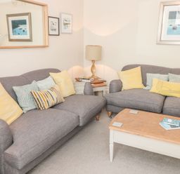 A living room with two gray sofas yellow and patterned cushions a wooden coffee table and framed pictures on the walls at Leylands in Salcombe