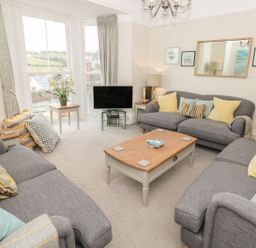 A living room with three gray sofas cushions a wooden coffee table and a television at Leylands in Salcombe