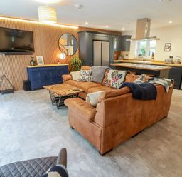 An open living room and kitchen with a brown leather sectional sofa a wooden coffee table a blue cabinet wall-mounted TV and a fireplace at The Grove in Wolfsdale near Haverfordwest