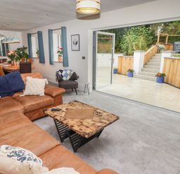A living room with a leather sofa and wooden coffee table next to an open patio door leading to a tiled outdoor area at The Grove in Wolfsdale near Haverfordwest