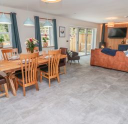 An open plan living and dining area with a wooden dining table and chairs a brown leather sofa a wall mounted television and sliding glass doors at The Grove in Wolfsdale near Haverfordwest