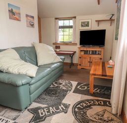 A living room with a sofa and television at Horseshoe Cottage near Holywell Bay