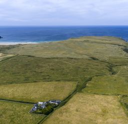 An aerial view of grassland and ocean at Horseshoe Cottage near Holywell Bay