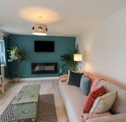 A living room with a sofa cushions a wooden coffee table a wall-mounted television and a fireplace at Villa Rose in Beadnell near Seahouses