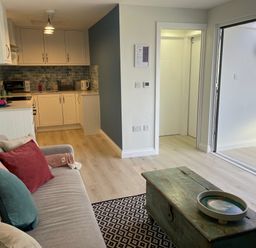 A living room with sofa and cushions small kitchen area and sliding glass door at Villa Rose in Beadnell near Seahouses